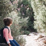 child carrying backpack sitting on a rock